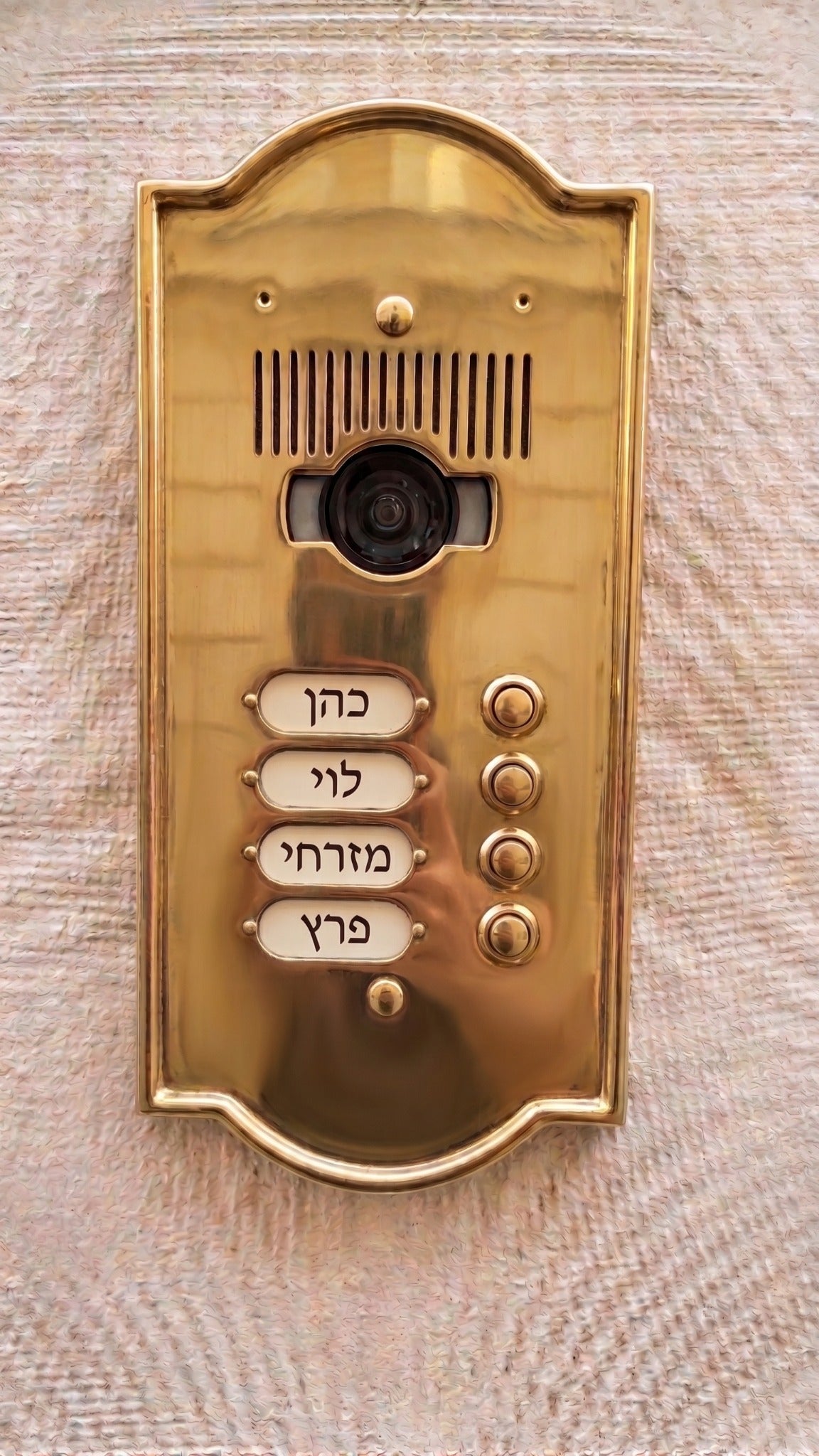 פאנל אינטרקום מוזהב עם מצלמה וארבעה לחצני קריאה על קיר בהיר