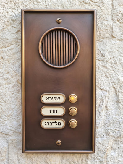 פאנל אינטרקום כהה עם רמקול עגול ושלושה לחצני קריאה על קיר אבן